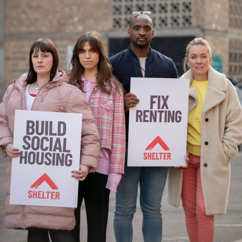 Three women and a man stand holding signs reading 'Build social housing' and 'fix renting'
