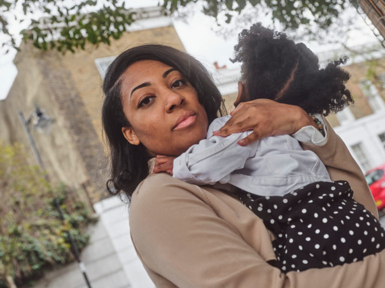 A woman holding a toddler looks at the camera