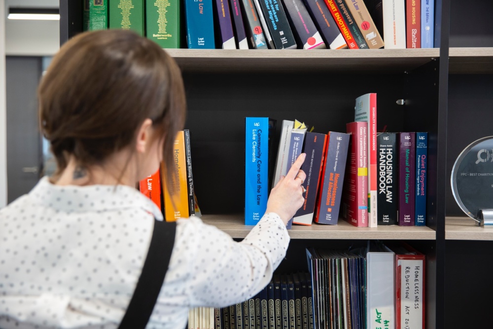 A woman removing a book from a bookcase. The books on the bookcase are about housing law. 