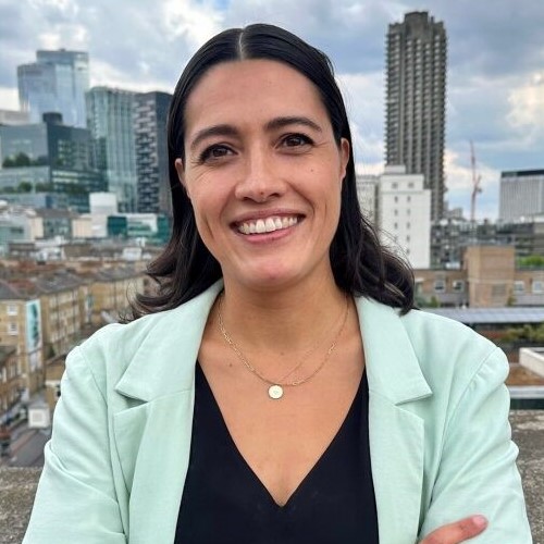 Mairi MacRae, Director of Communications, Policy and Campaigns, stands on the roof terrace of Shelter's London office with city buildings in the background.