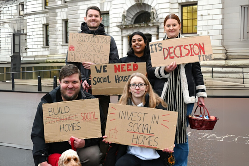 A group of Shelter colleagues standing outside the Treasury building in London holding cardboard signs which read 'it's decision time', and 'invest in social homes'.