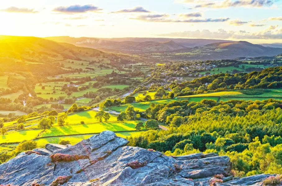 A beautiful view of the Peak District at sunset, with two hills covered in trees and green fields
