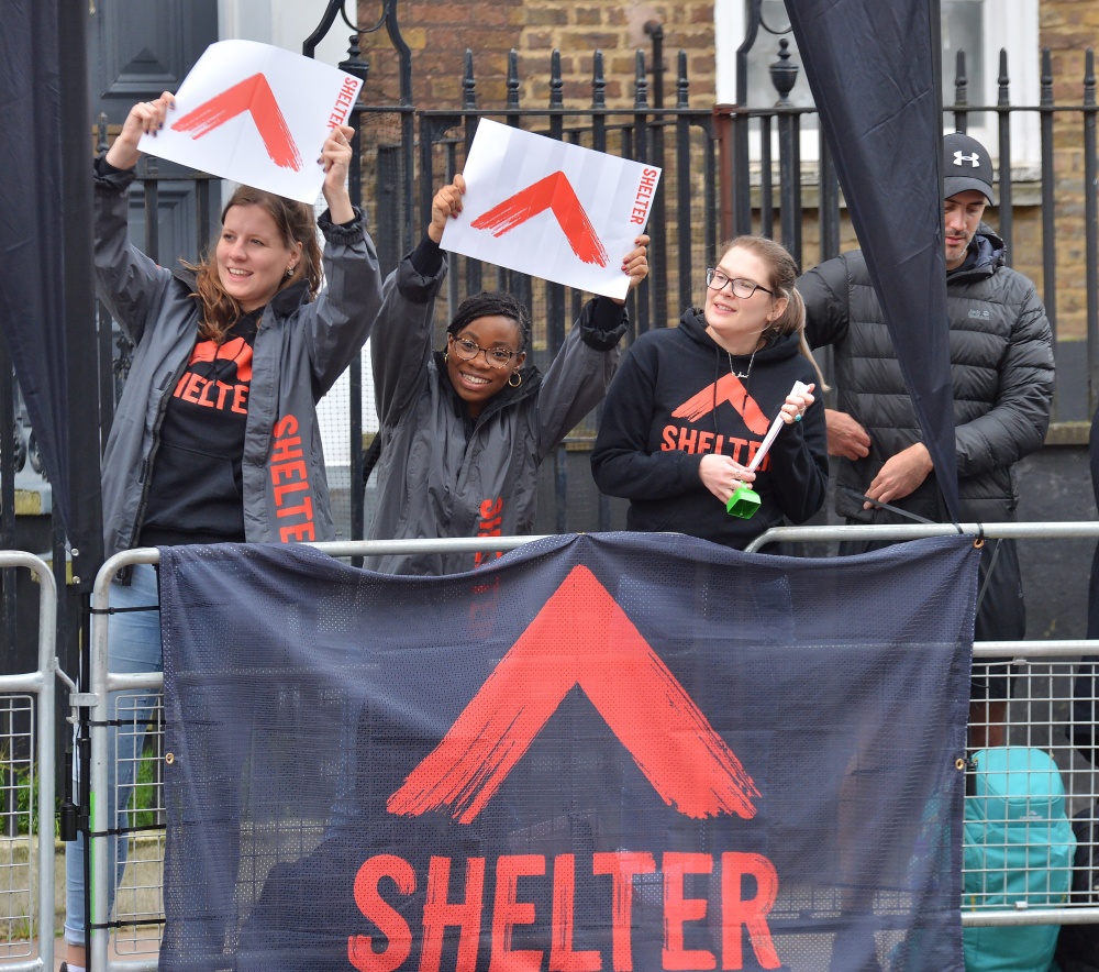 Three women wearing Shelter jumpers raising posters in support of Shelter marathon runners 