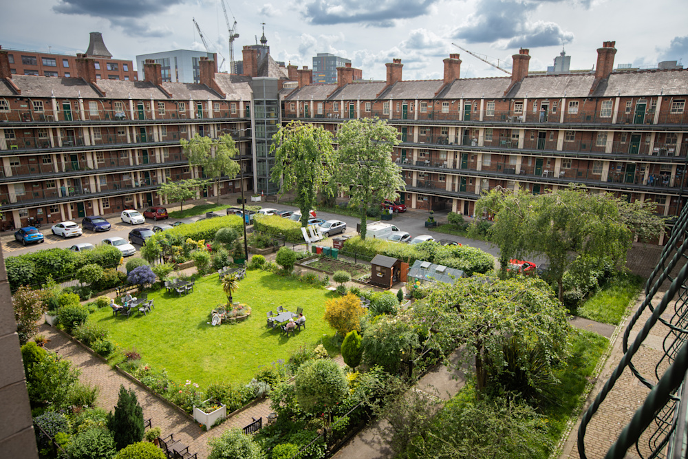 A view looking down on two square blocks of social housing, with cars parked around the edge and a green in the middle. City buildings are visible in the background.