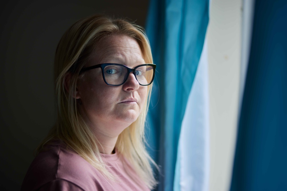 A women called Vicky by blue curtains looking forward at the camera 