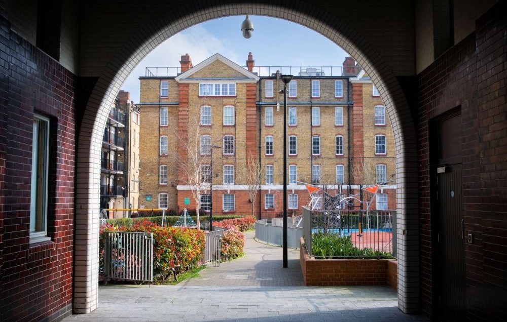 View through an archway into the courtyard of an attractive social housing development, with a red and yellow brick block of flats.