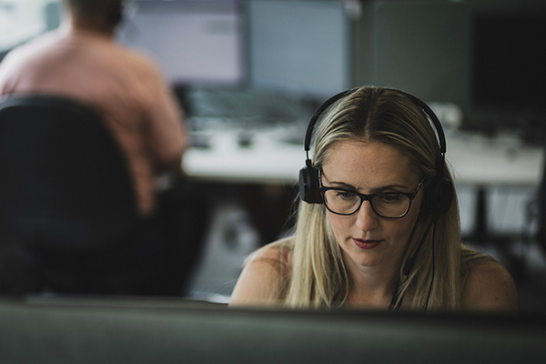 A woman wearing a telephone headset is sat front of a computer in a Shelter office.
