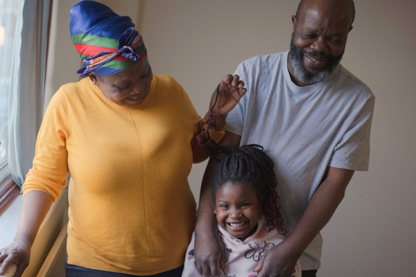 Two smiling parents and their child, stood at the window of their social home.