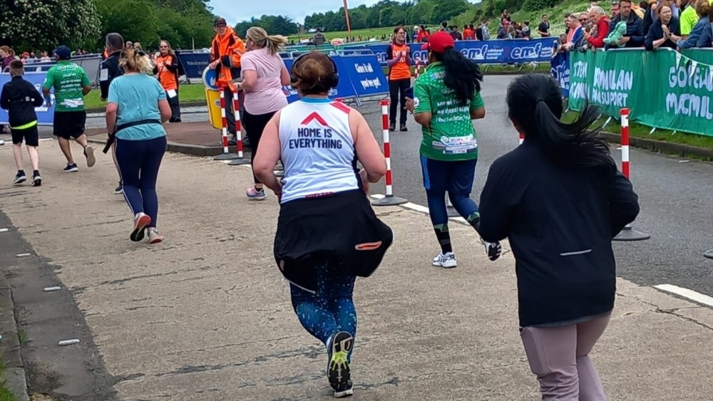 A woman running in a Shelter vest which says 'Home is everything' on the back