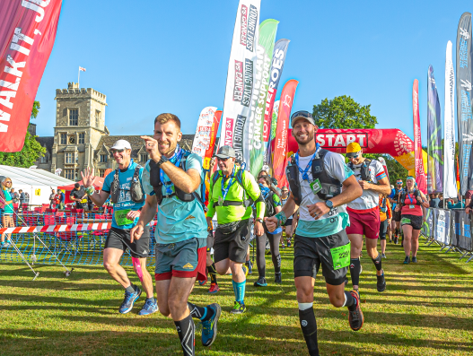 A group of joggers leaves the start line on a sunny day - in the background are banners and an impressive castle