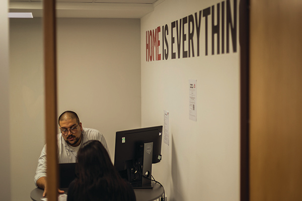 A man sat behind a computer in a Shelter office, speaking to a woman