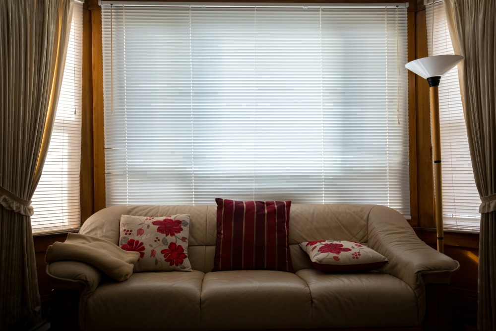 A cosy home interior, showing a sofa with floral cushions and a window with drawn blinds in the background.