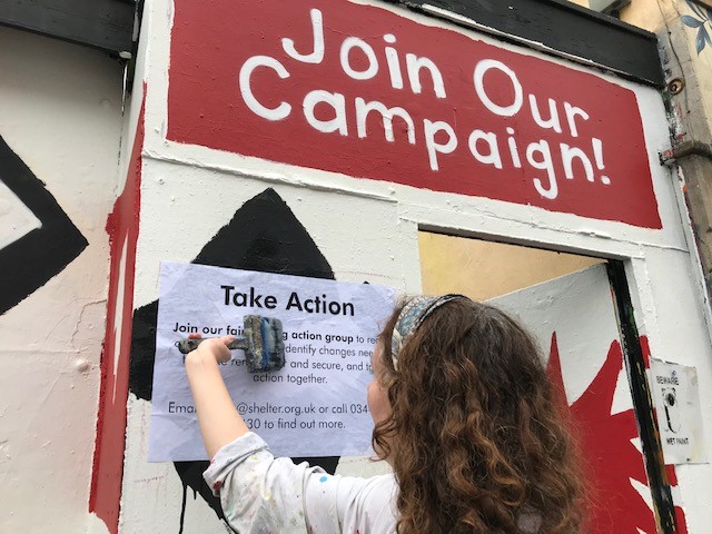 A campaigner pasting a 'take action' sign onto a wall.