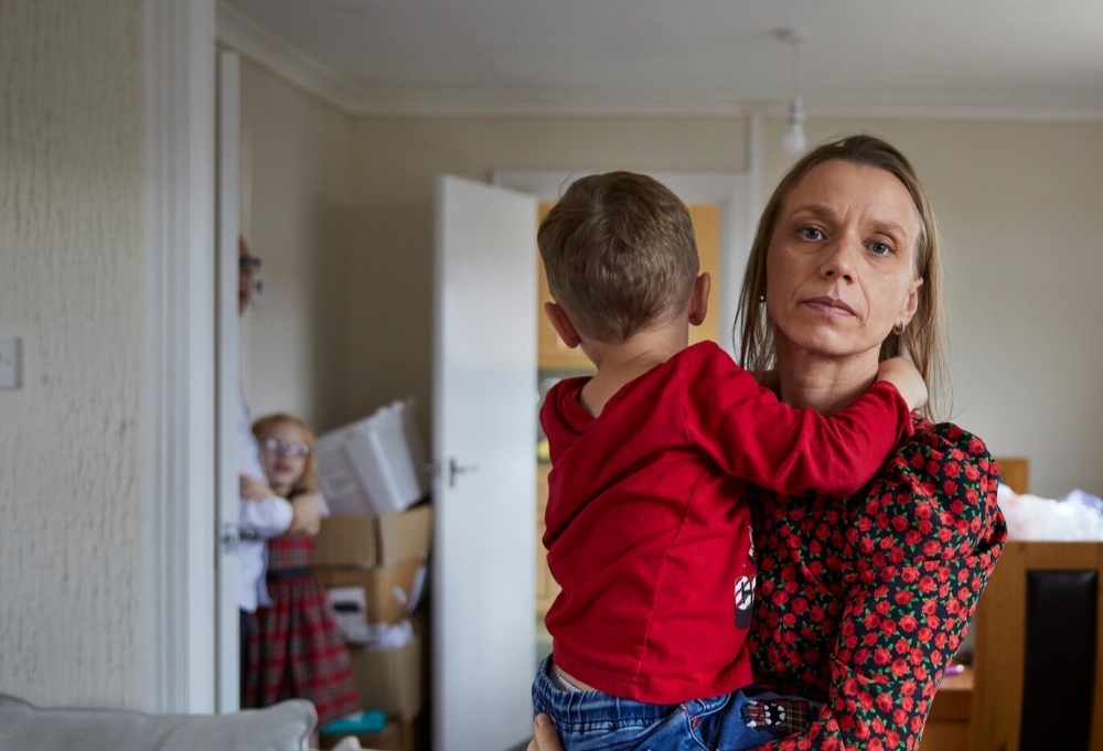 A woman holds her baby with a toddler in the background