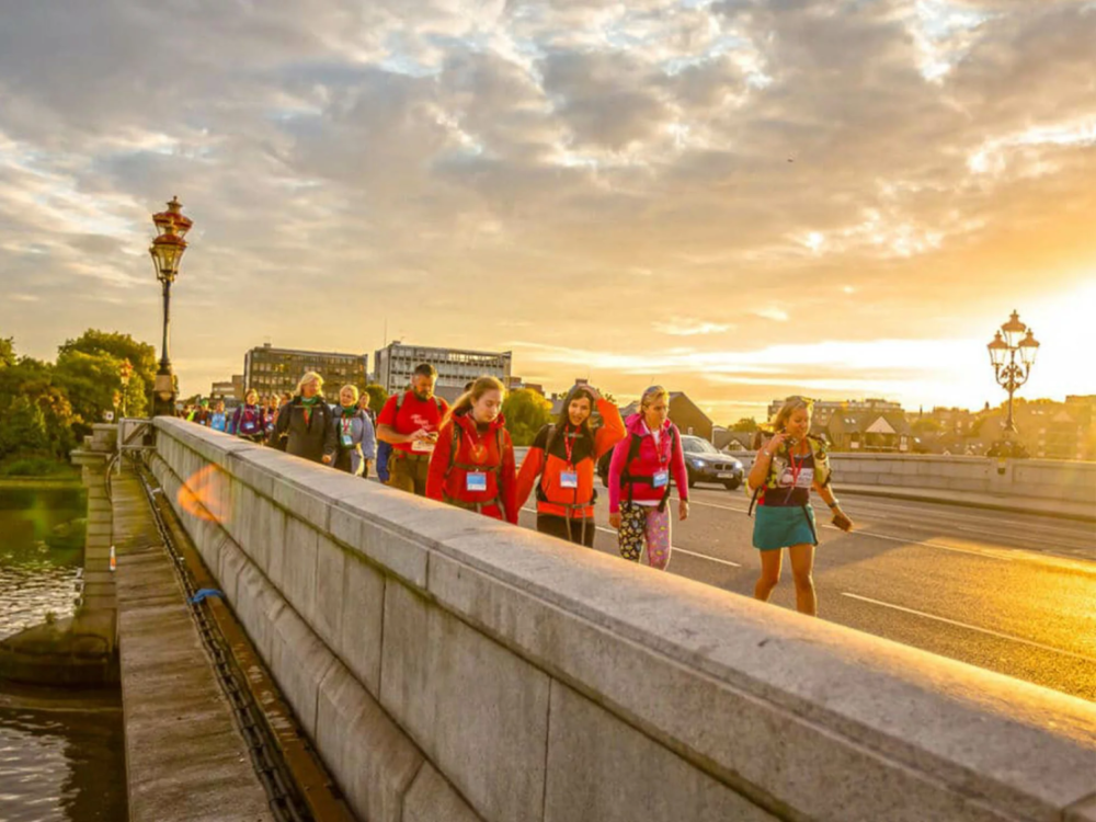A group of walkers on a bridge in London, with the sun rising in the background.
