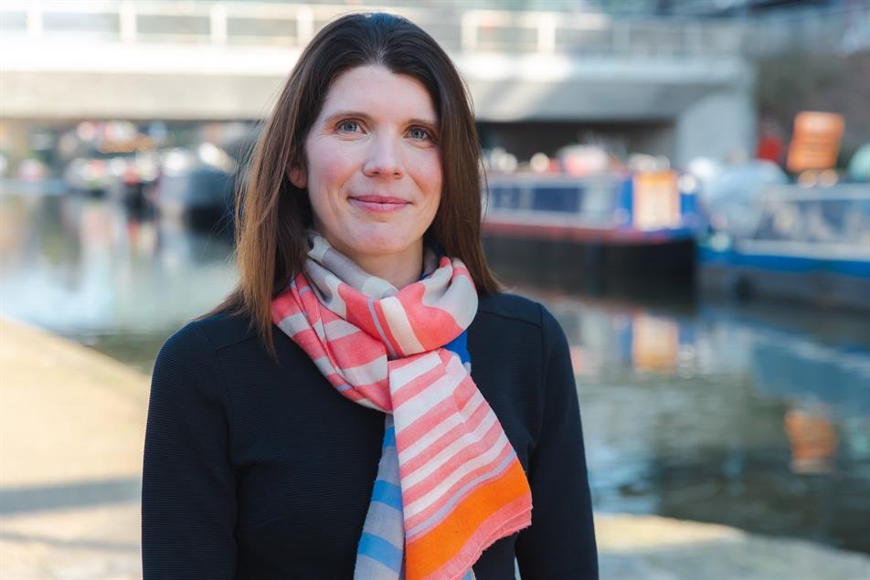 Shelter's CEO Sarah Elliot wearing a colourful scarf and smiling at the camera, with a river in the background.