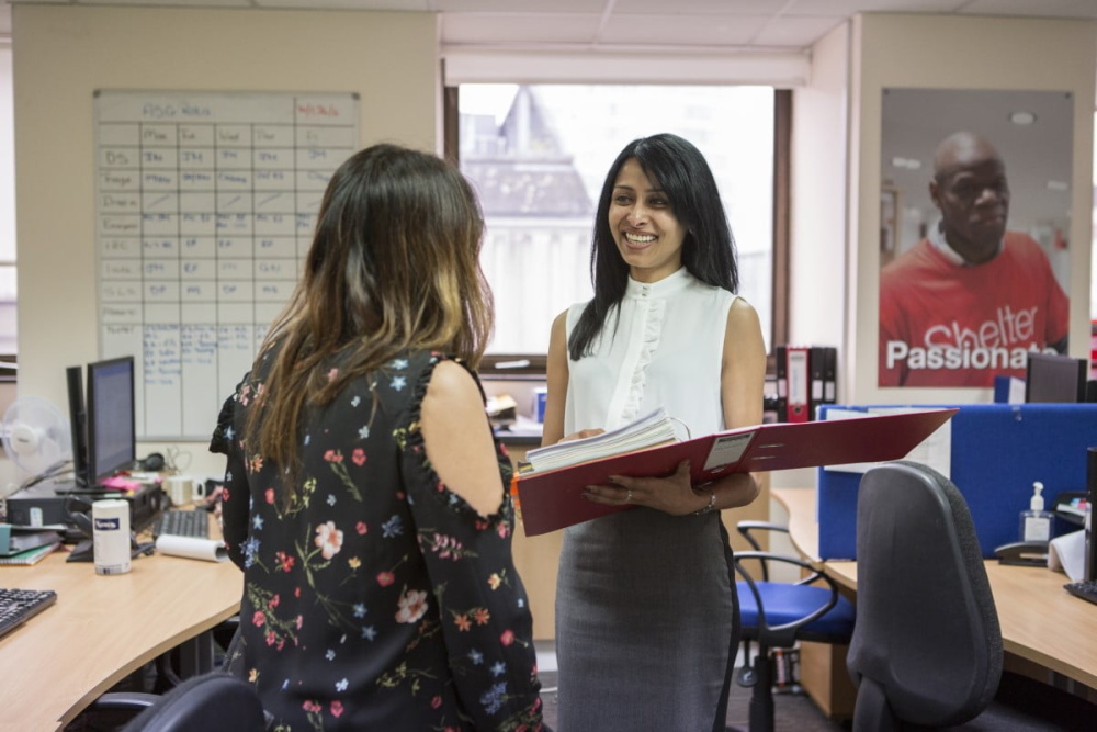 Two women stand talking in an office