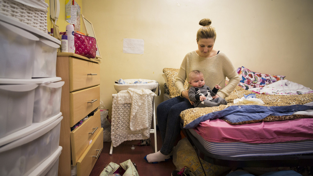 Francesca holds her baby on a camp bed set up in a bare room