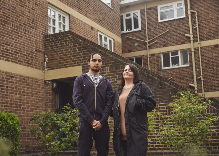 A mother and son stand outside a block of flats.