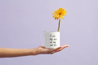 Yellow flower in a mug on a stretched out hand with purple background