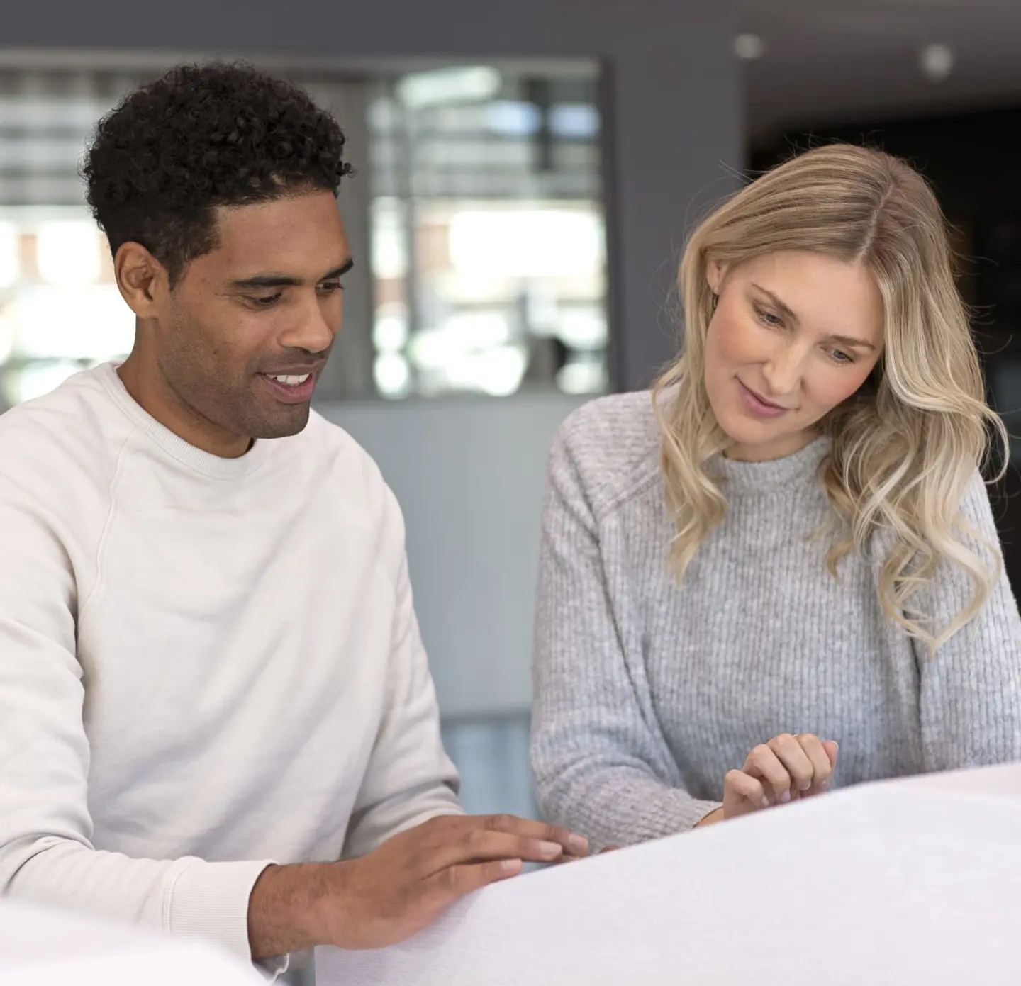 A young couple facing forward and looking down at a screen, smiling.