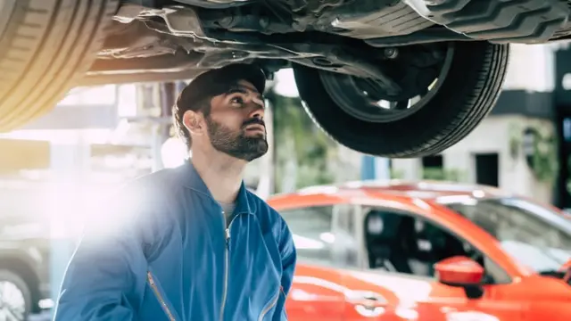 Male car mechanic checking under car