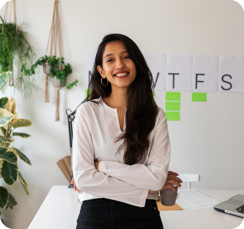 Une jeune femme souriante dans un bureau à domicile. Son ordinateur portable et ses documents sont bien visibles sur le bureau.