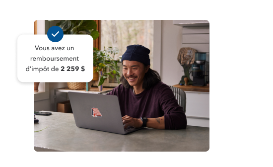Un jeune homme souriant qui travaille sur son ordinateur portable chez lui. Illustration secondaire avec le texte et le crochet « Votre remboursement d’impôt est de 2 259 $ ».