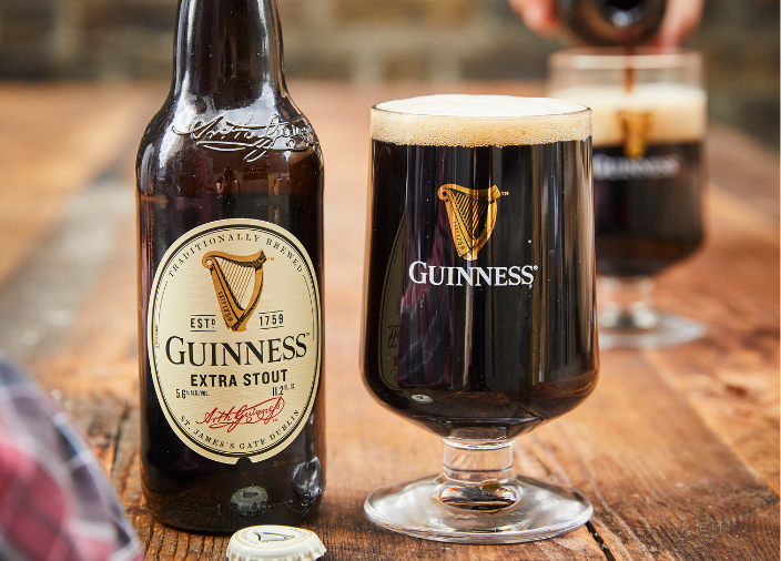 Eine Flasche Guinness Extra Stout auf einem Tisch neben einem mit Guinness gefüllten Pintglas.