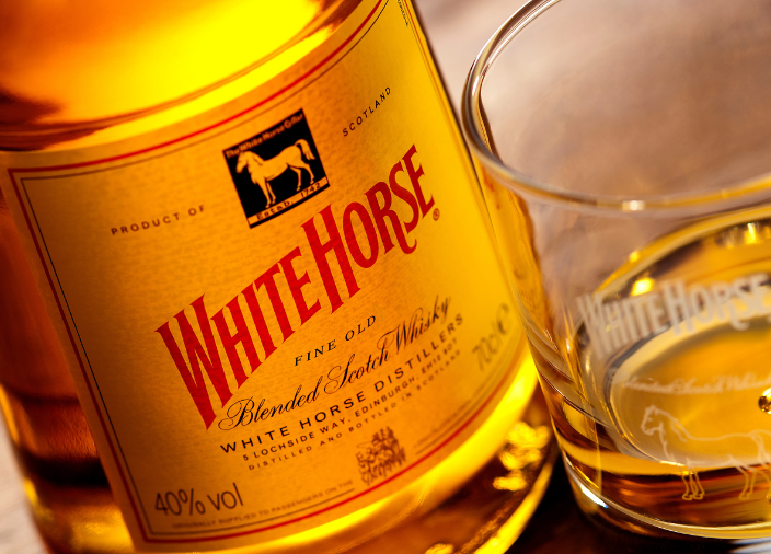 Eine Flasche White Horse Whisky auf einem Tisch neben einem Glas Whisky