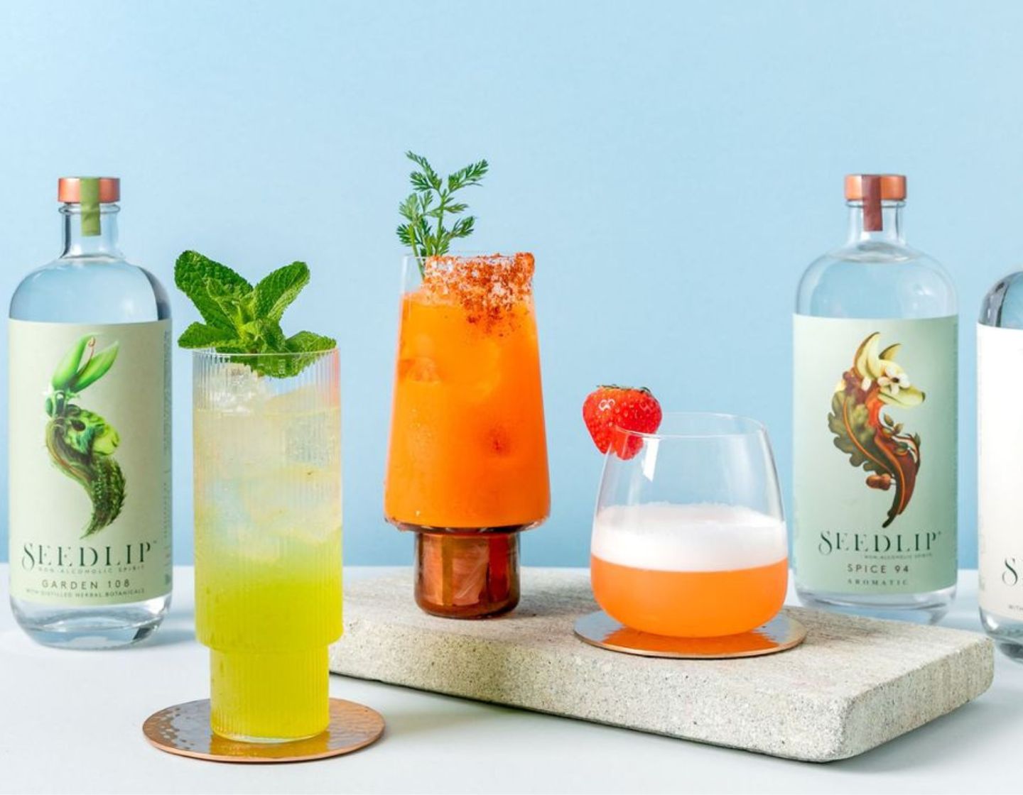  3 cócteles en vasos tumbler junto a botellas de Seedlip