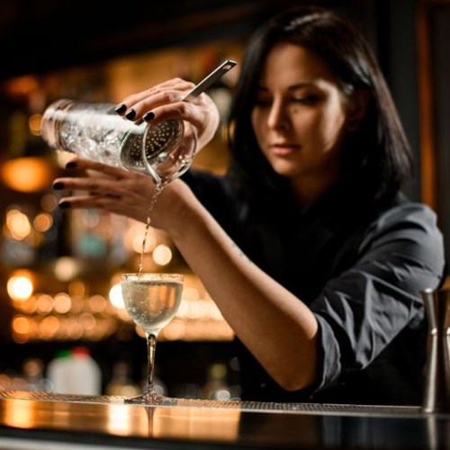 Female bartender straining cocktail into glass on bar