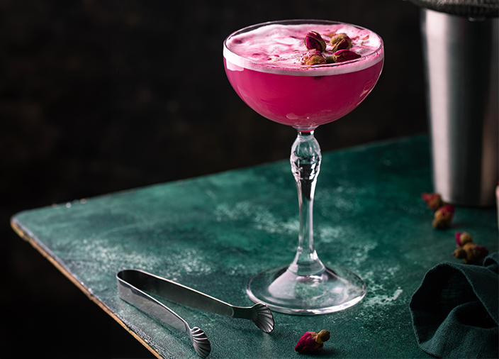  Image alt Text   Una copa de cóctel de champán clásica con un cóctel rosa brillante, la capa superior de espuma está decorada con flores. 