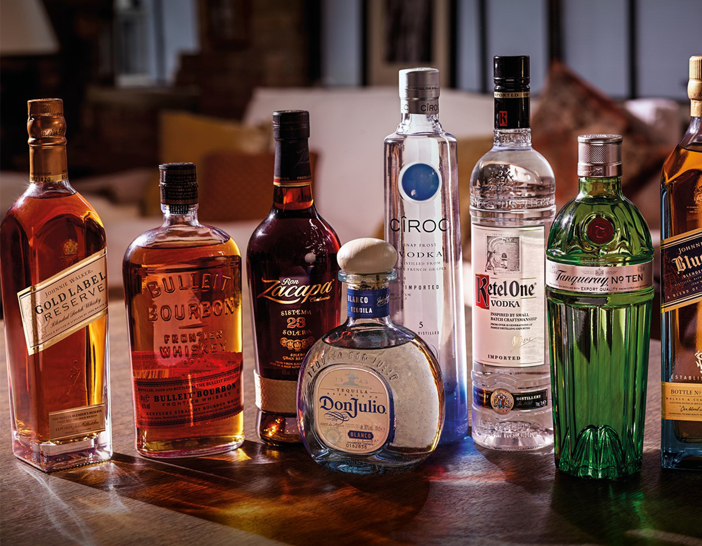 Um grupo de garrafas de bebida, da esquerda para a direita, Johnnie Walker Gold Label Reserve, Bulleit Bourbon, Zacapa, Don Julio, Cîroc, Ketel One, Tanqueray N° Ten e Johnnie Walker Blue Label. 