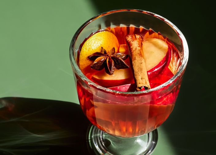 Ein roter Cocktail mit einer Zimtstange, geschnittenen Äpfeln und Nelken.