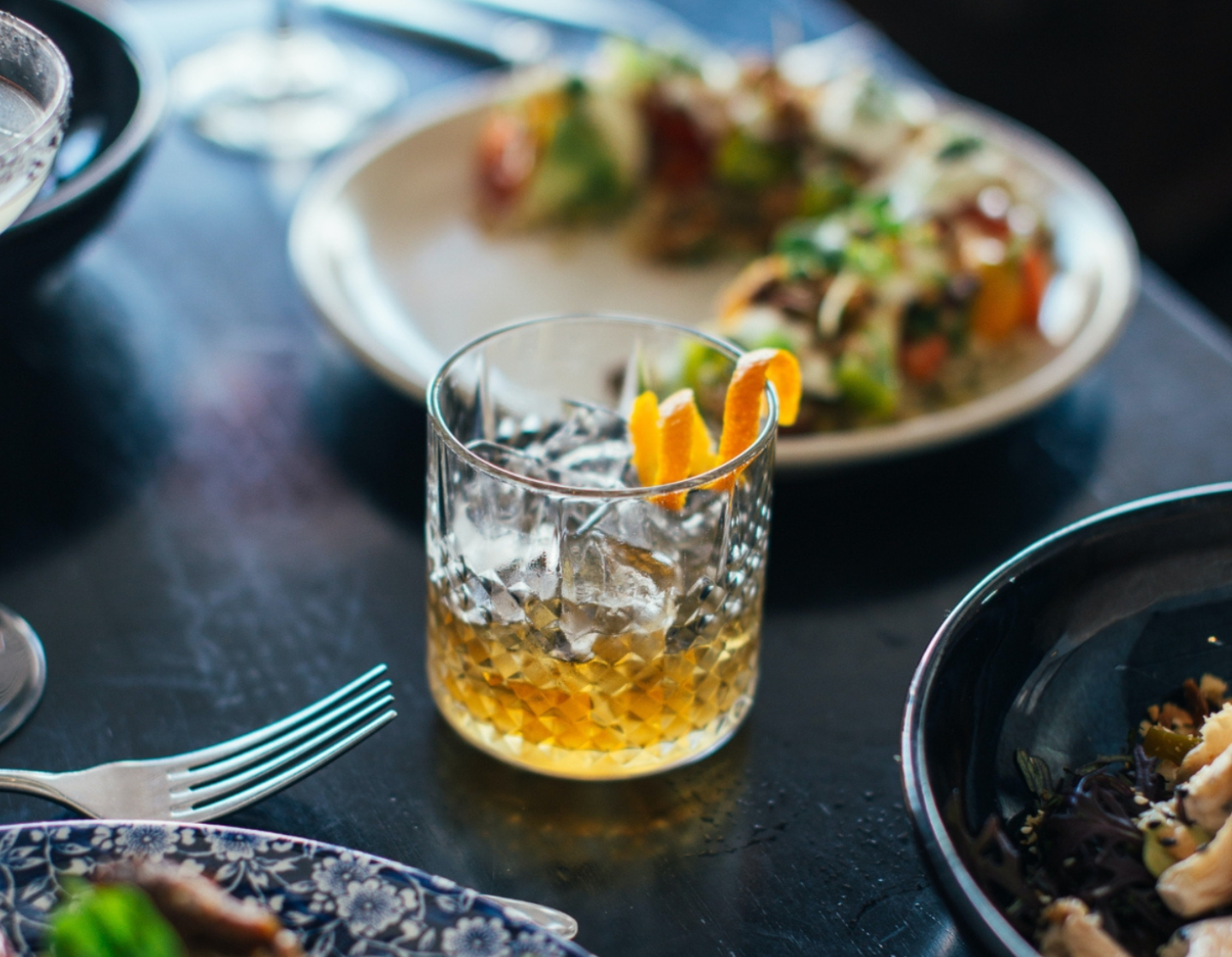 Copo cheio de whisky com pratos de comida ao fundo