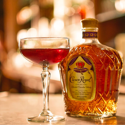 Botella de whiskey Crown Royal en la mesa alrededor de un cóctel en copa coupe.