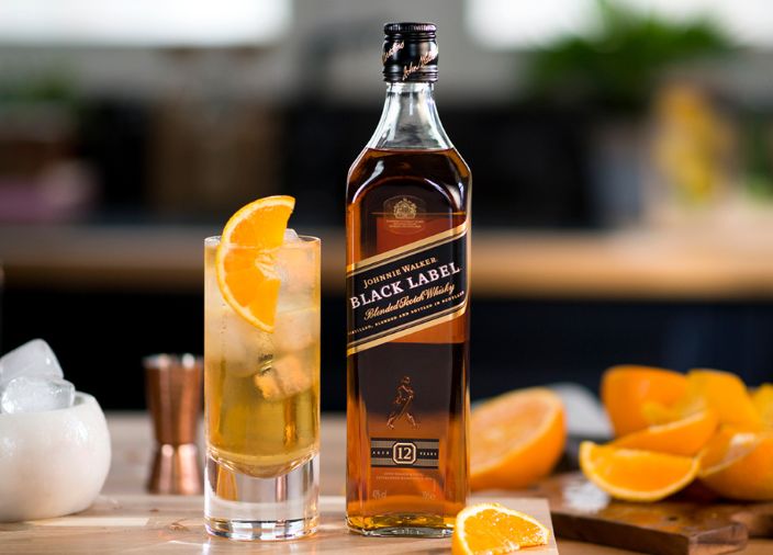 Eine Flasche Johnnie Walker Black Label neben einem Whisky Glas mit einem Whisky Cocktail und Eis