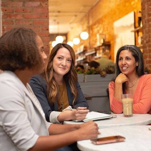 3 Personen sitzen an einem Tisch mit Stift und Papier und unterhalten sich