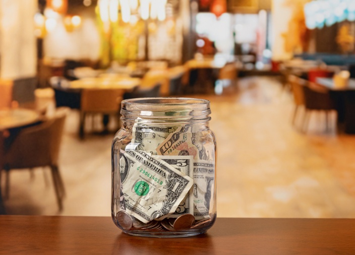 A close-up shot of a tip jar stuffed with notes and coins in a bar-restaurant.