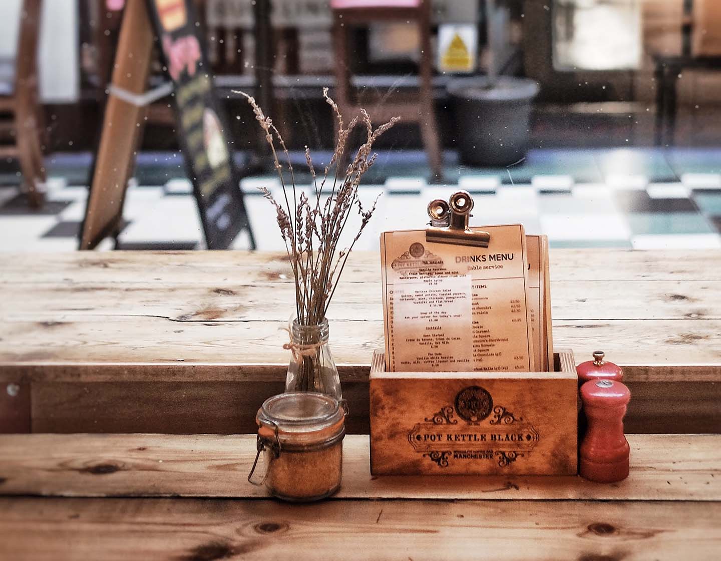 A drinks menu sits on a wooden counter with a plant and salt and pepper beside it.