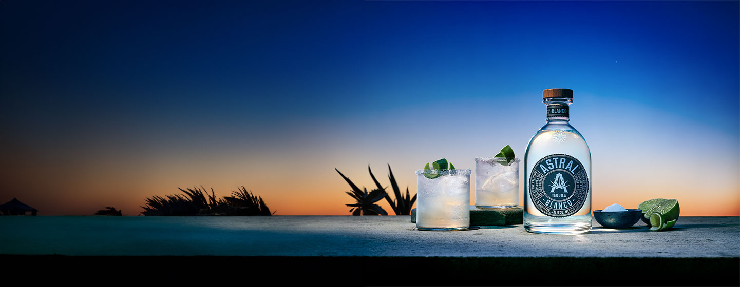 Bottle of Astral with two cocktails in front of landscape