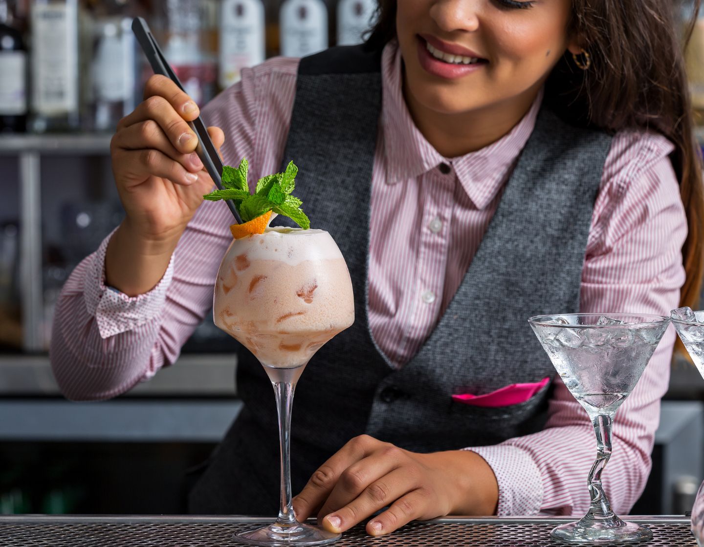 Ein Barkeeper garniert einen gefrorenen Cocktail mit Minze und Orange. 