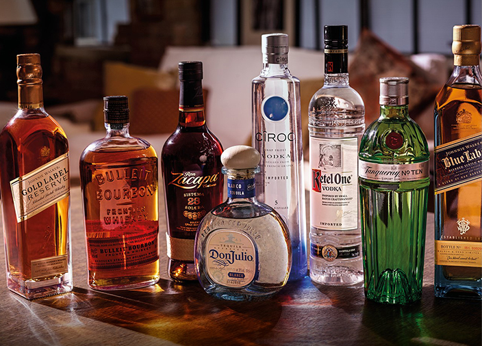 Um grupo de garrafas de bebida, da esquerda para a direita, Johnnie Walker Gold Label Reserve, Bulleit Bourbon, Zacapa, Don Julio, Cîroc, Ketel One, Tanqueray N° Ten e Johnnie Walker Blue Label.