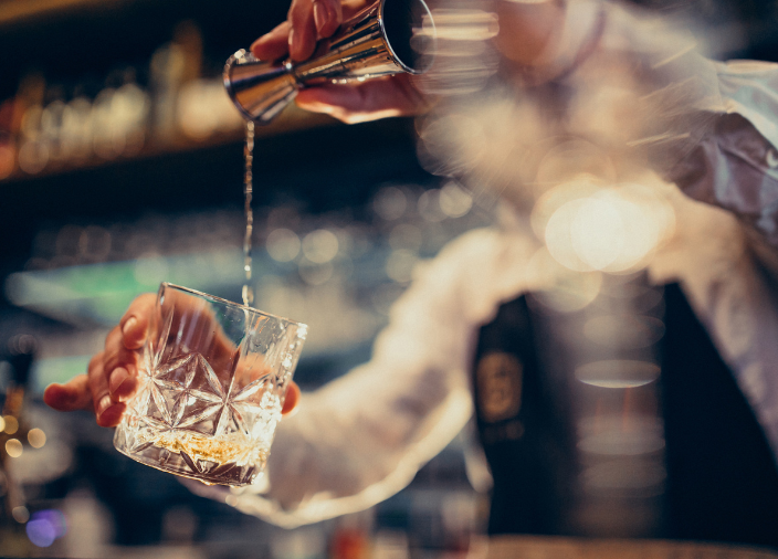 Imagem de um bartender colocando líquido no copo usando um dosador