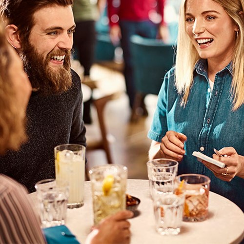 Bartender sonriente interactuando con clientes que disfrutan de bebidas en una mesa