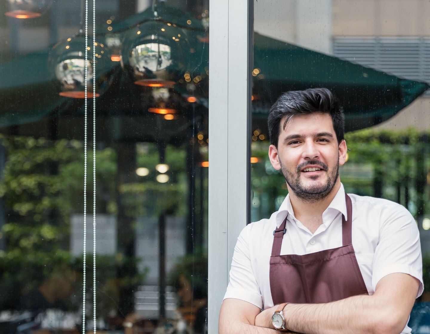 Bartender in apron leans against glass window of venue
