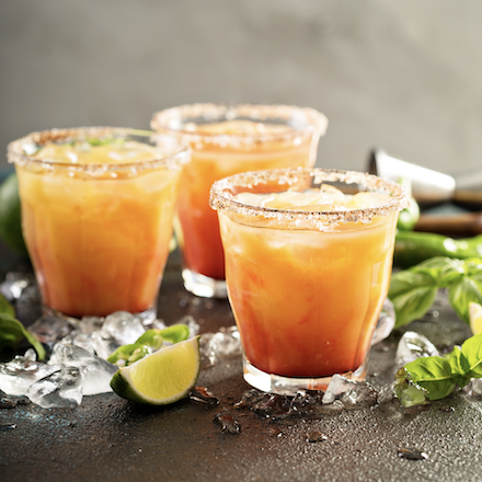 Three margarita cocktails of orange colour with salt rim