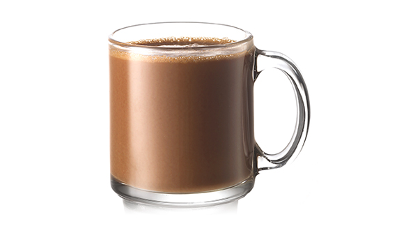 Uma bebida Talisker Campfire Hot Chocolate, ao lado de uma garrafa de uísque Talisker, em uma mesa em frente a uma poltrona e fogueira alta. 