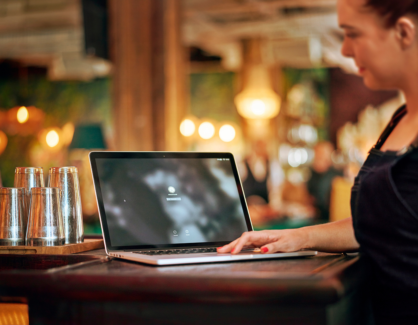 Woman standing in a bar setting holding a laptop